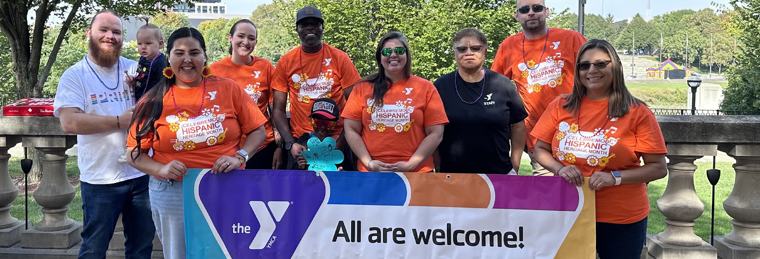 Group of people holding a banner with a YMCA logo that reads All Are Welcome
