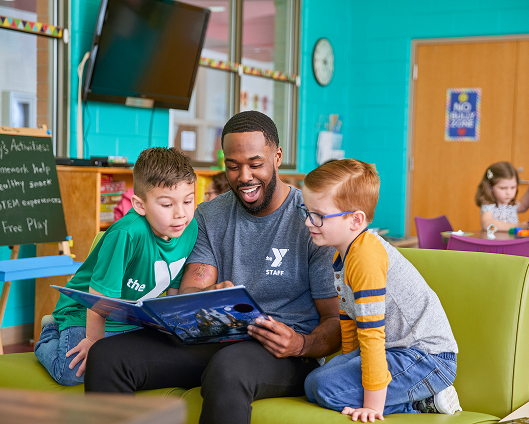 A YMCA teacher reading a story to two youth.