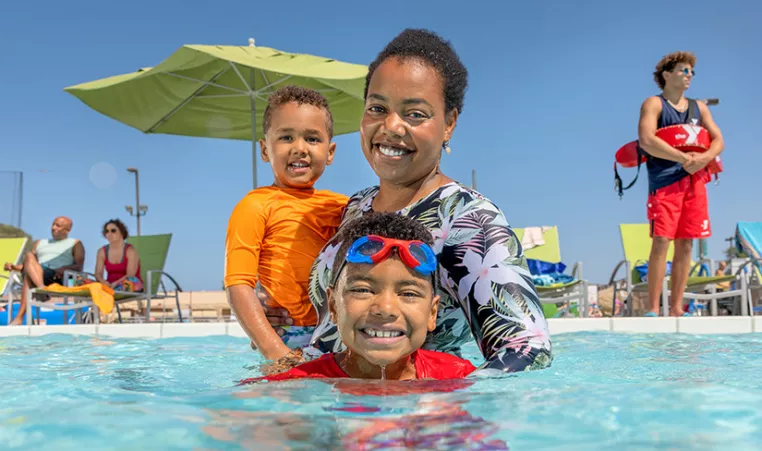 adult and children swimming in an outdoor pool with a lifeguard behind them