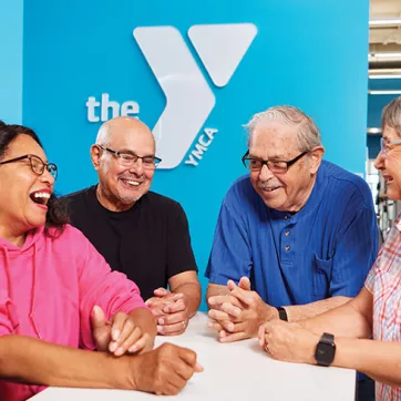 Group of adults laughing with the YMCA logo behind them