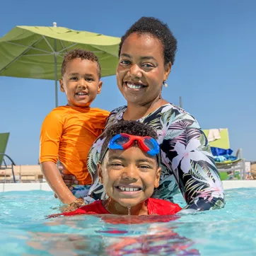 adult and children swimming in an outdoor pool with a lifeguard behind them